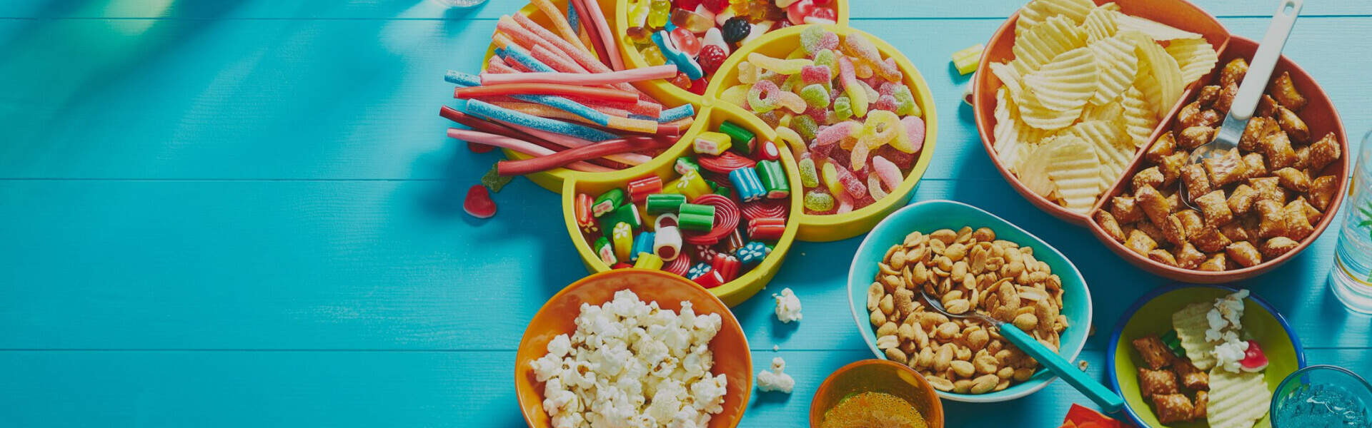 Aqua table surface with variety of movie snacks: popcorn, sweet and sour candy, chips, pretzel bites and flavoured sparkling water