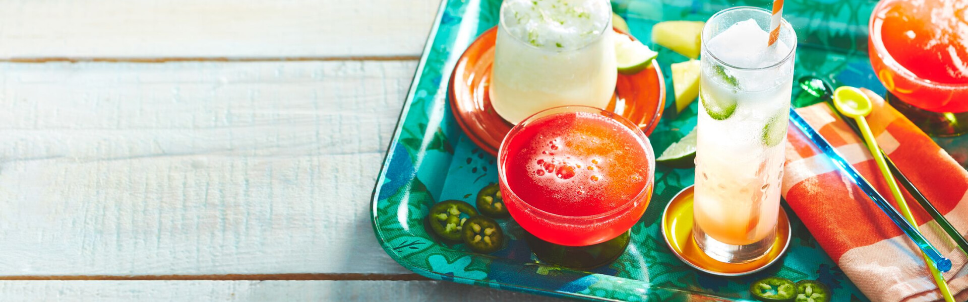 Three fizzy summer drinks made with flavoured sparkling water on a marbled aqua serving platter over a white-washed wooden table surface