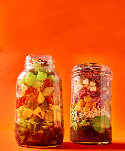 two large jars of layered salad on an orange background