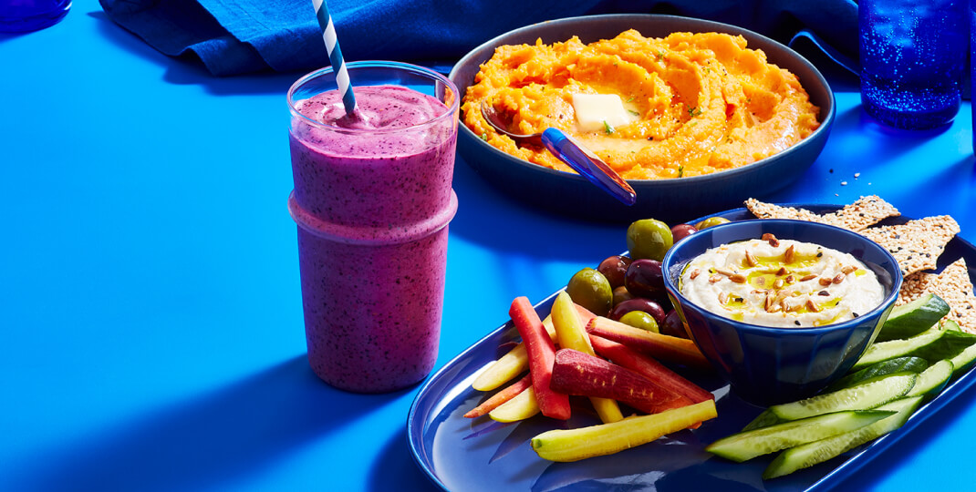 Glass with cauliflower smoothie, with sweet poato mash, and hummus in background