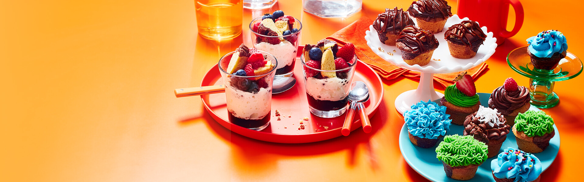 Brownie Madeleine trifle cups, caramel brownie Madeleine, and mini brownie Madeleine cupcakes on an orange backdrop