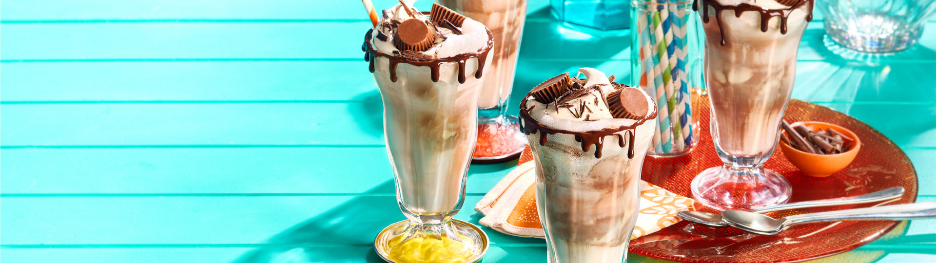 Quatre flotteurs à la crème glacée au chocolat et au beurre d’arachide dans de grands verres avec pailles et cuillères.