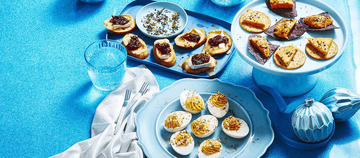 Cheese ball 'n' chips on a white cake stand, brie 'n' cranberries on a blue serving tray and devilled eggs 'n' cheese on a blue plate.